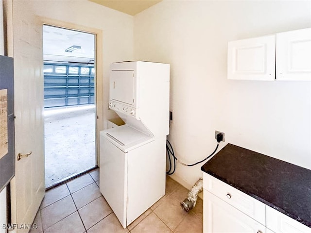 laundry room featuring stacked washer and dryer, cabinets, and light tile patterned floors