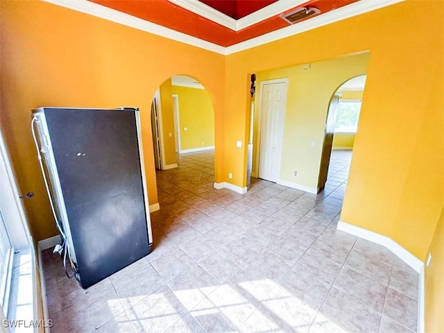 empty room with arched walkways, ornamental molding, light tile patterned floors, and baseboards