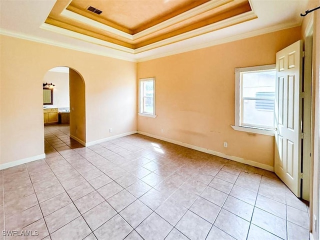 empty room featuring a tray ceiling, light tile patterned floors, crown molding, arched walkways, and baseboards