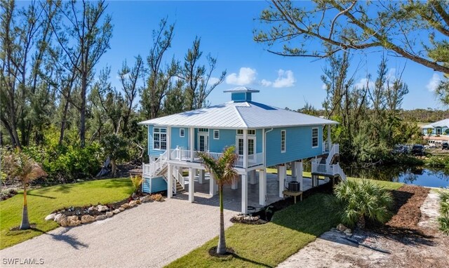 coastal home with a carport, a front lawn, a water view, and french doors