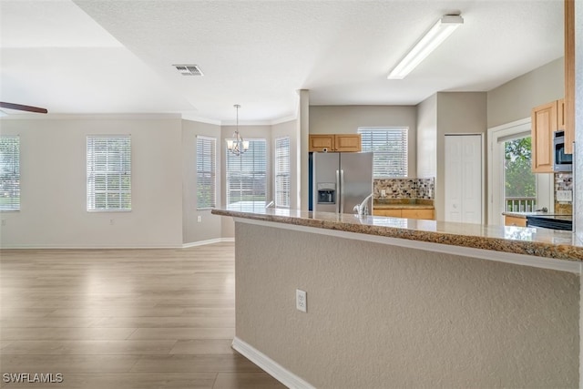 kitchen with hanging light fixtures, light brown cabinetry, appliances with stainless steel finishes, light hardwood / wood-style floors, and light stone counters