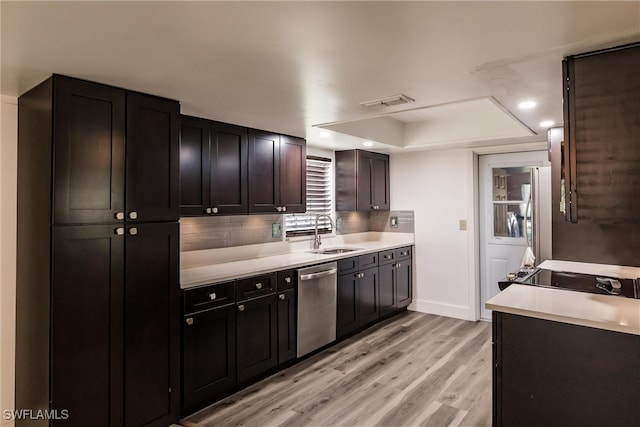 kitchen featuring stainless steel appliances, sink, backsplash, a tray ceiling, and light wood-type flooring