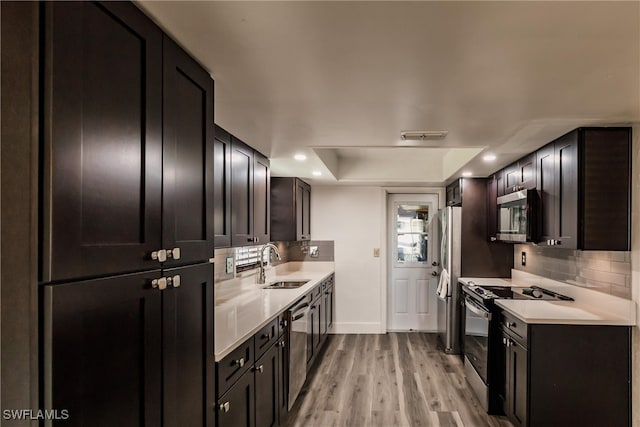 kitchen featuring tasteful backsplash, stainless steel appliances, sink, light hardwood / wood-style floors, and a tray ceiling