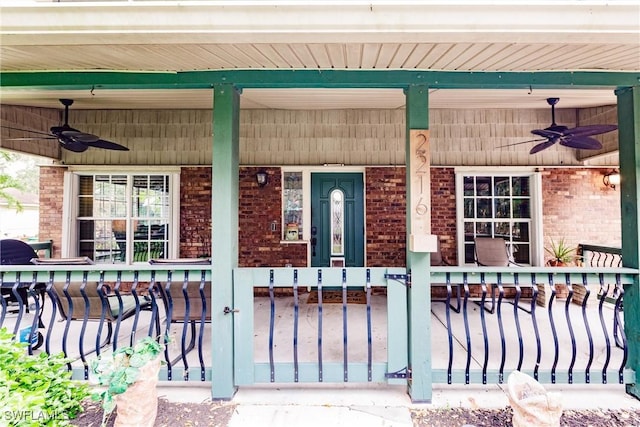 view of exterior entry featuring a porch, a ceiling fan, and brick siding