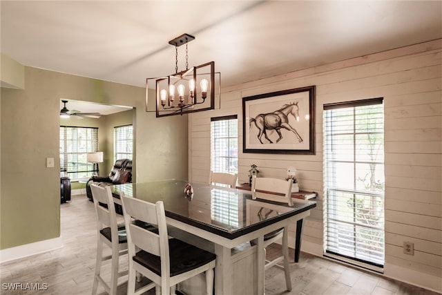 dining area featuring ceiling fan with notable chandelier, wooden walls, and light wood-type flooring