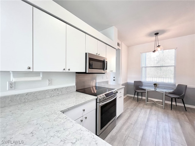 kitchen with stainless steel appliances, white cabinets, pendant lighting, and light hardwood / wood-style flooring