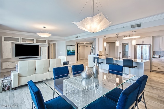 dining area featuring sink, ornamental molding, and light hardwood / wood-style flooring