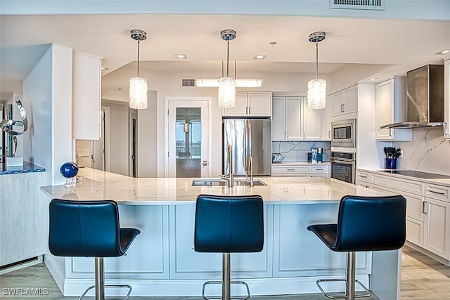 kitchen with appliances with stainless steel finishes, a kitchen breakfast bar, light stone countertops, wall chimney exhaust hood, and white cabinets