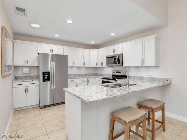 kitchen with light stone countertops, a breakfast bar, stainless steel appliances, light tile patterned floors, and white cabinets