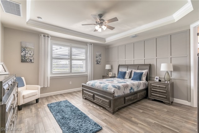 bedroom featuring a tray ceiling, ceiling fan, ornamental molding, and light wood-type flooring