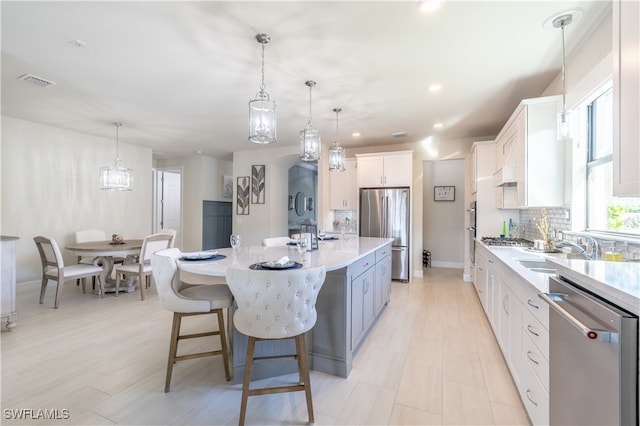 kitchen featuring a large island with sink, white cabinets, pendant lighting, and appliances with stainless steel finishes