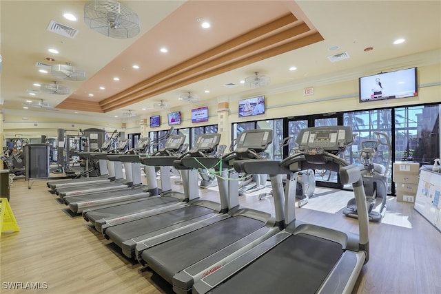 gym featuring a tray ceiling, light hardwood / wood-style flooring, and ceiling fan