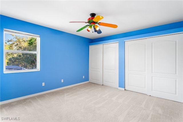 unfurnished bedroom with ceiling fan, light carpet, and two closets