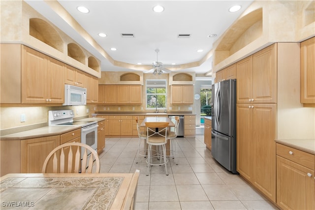 kitchen with light tile patterned flooring, light brown cabinets, a kitchen island, and stainless steel appliances