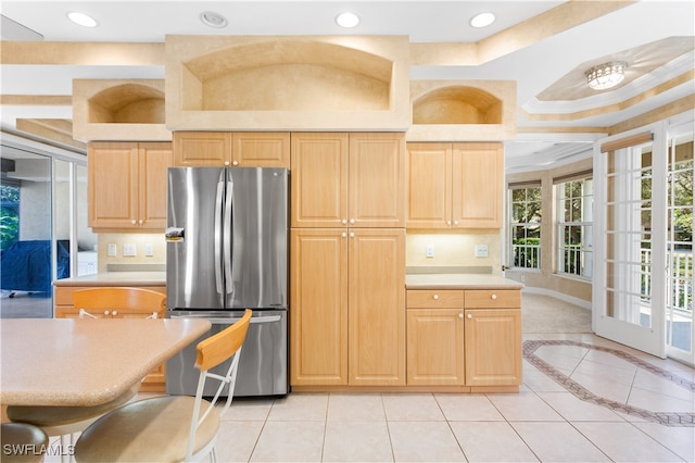 kitchen featuring stainless steel refrigerator, crown molding, a kitchen bar, light brown cabinetry, and light tile patterned floors