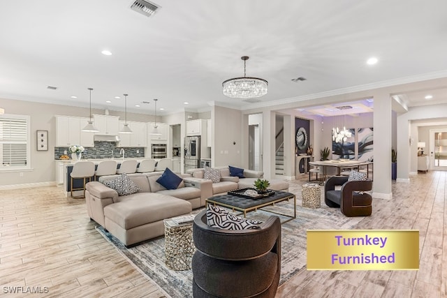 living room with a notable chandelier, light wood-type flooring, and ornamental molding