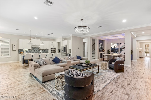 living room with crown molding, light wood-type flooring, and an inviting chandelier