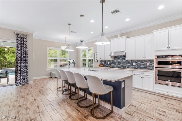 kitchen featuring white cabinetry, sink, an island with sink, and decorative light fixtures