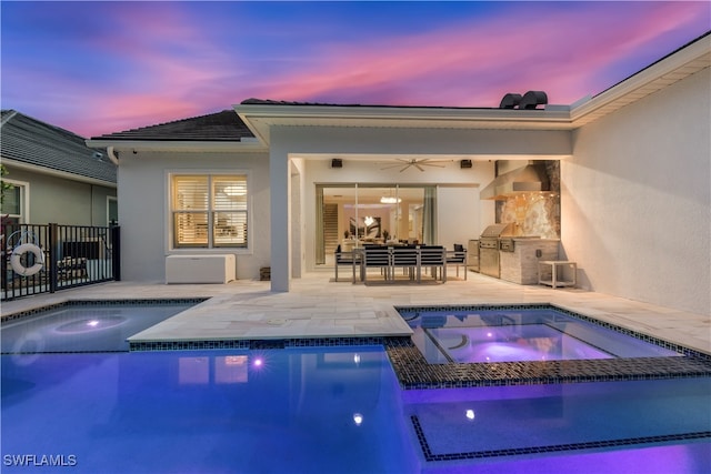 pool at dusk with an outdoor kitchen, ceiling fan, a patio area, and an in ground hot tub