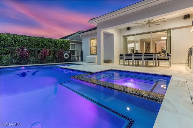 pool at dusk featuring ceiling fan, an in ground hot tub, and a patio