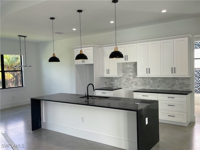 kitchen with hanging light fixtures, white cabinets, sink, and a kitchen island with sink