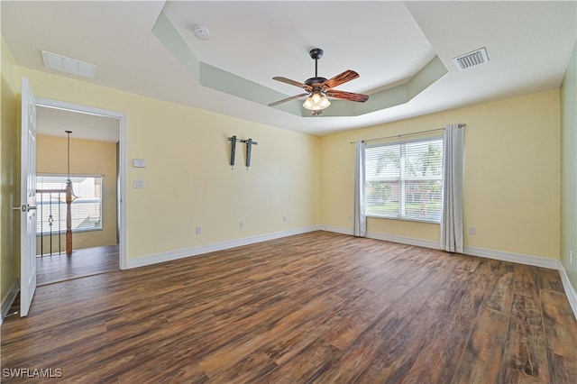 spare room with dark hardwood / wood-style floors, a raised ceiling, and ceiling fan with notable chandelier