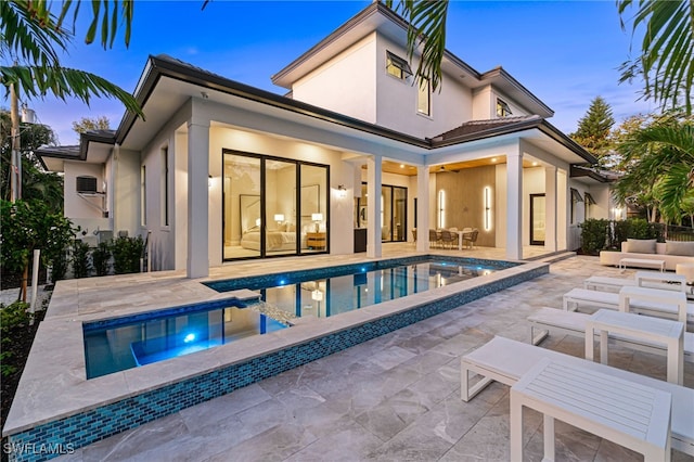 back house at dusk featuring outdoor lounge area, a pool with hot tub, and a patio