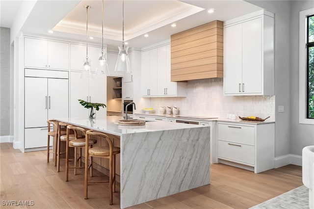 kitchen with paneled fridge, a center island with sink, and white cabinetry