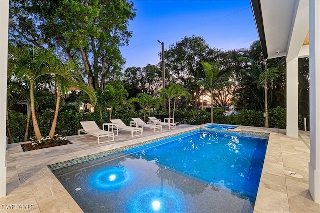 pool at dusk featuring an in ground hot tub and a patio