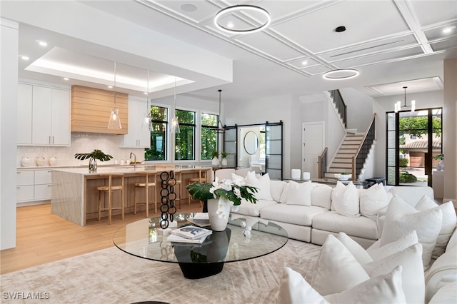 living room with a barn door, a healthy amount of sunlight, coffered ceiling, and light hardwood / wood-style floors