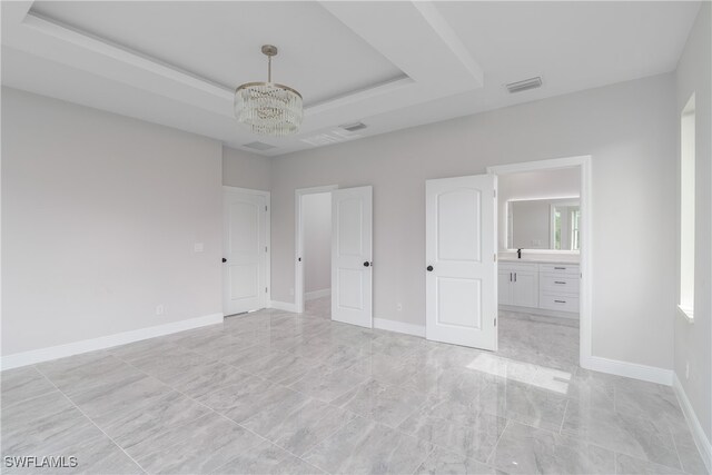 unfurnished bedroom featuring ensuite bath, a raised ceiling, and a notable chandelier