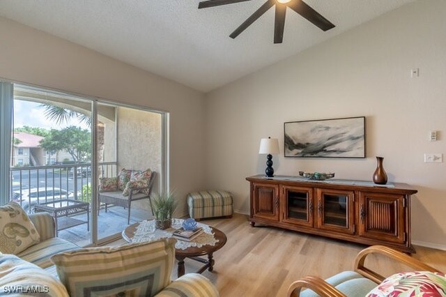 living room featuring ceiling fan, light wood-type flooring, a textured ceiling, and lofted ceiling