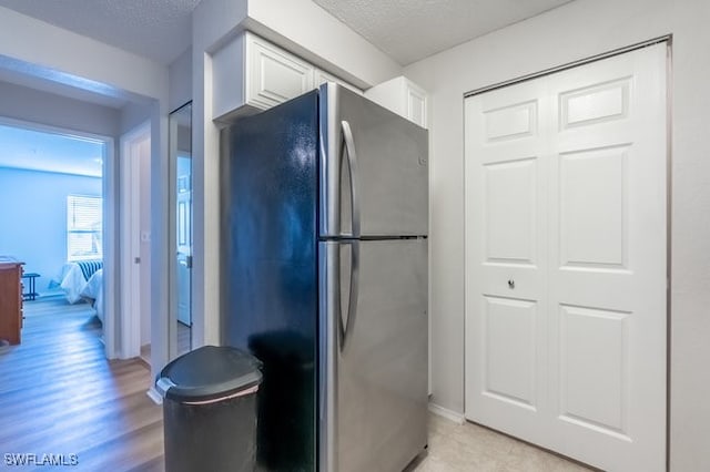 kitchen with stainless steel refrigerator, light hardwood / wood-style flooring, white cabinets, and a textured ceiling