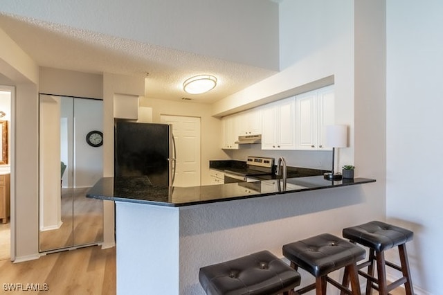 kitchen with white cabinets, black fridge, stainless steel electric range oven, light hardwood / wood-style floors, and kitchen peninsula