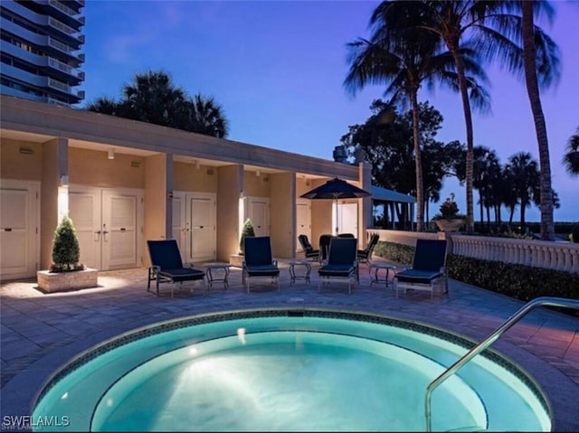 pool at dusk with a patio area and an in ground hot tub