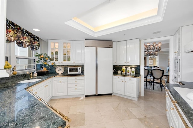 kitchen featuring tasteful backsplash, a raised ceiling, paneled built in fridge, and white cabinets