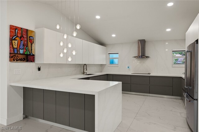 kitchen with white cabinetry, wall chimney exhaust hood, kitchen peninsula, and stainless steel refrigerator