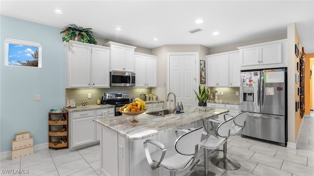 kitchen with stainless steel appliances, white cabinets, sink, a kitchen island with sink, and backsplash