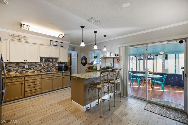 kitchen featuring crown molding, sink, dark stone countertops, hanging light fixtures, and a breakfast bar area