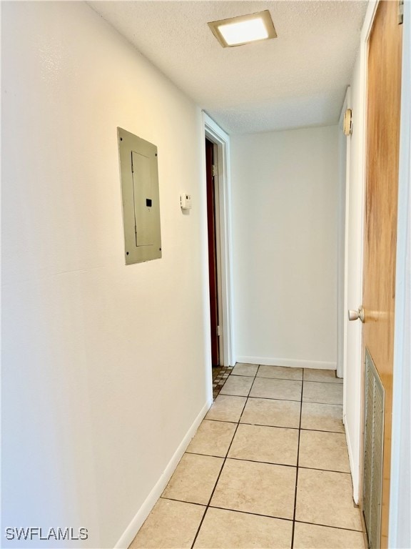 hall with a textured ceiling, electric panel, and light tile patterned flooring