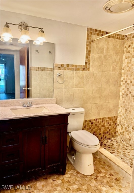 bathroom featuring vanity, toilet, tile walls, and tiled shower