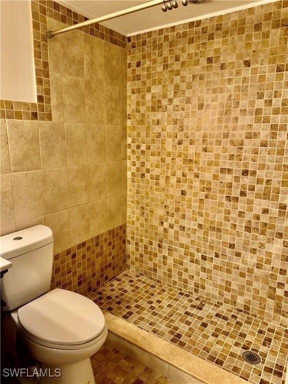 bathroom featuring tile patterned flooring, a tile shower, toilet, and tile walls