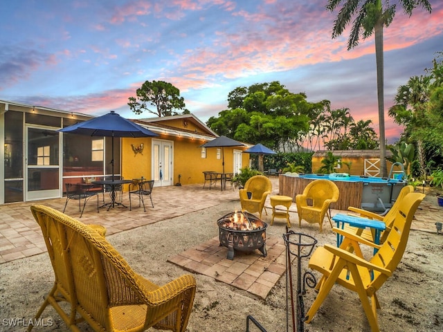 patio terrace at dusk featuring french doors, an outdoor fire pit, and a sunroom