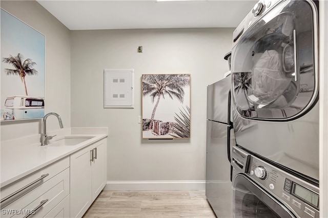 clothes washing area with cabinets, stacked washer and clothes dryer, sink, and light wood-type flooring