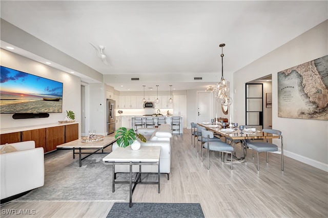 living room with light wood-type flooring, a chandelier, and sink