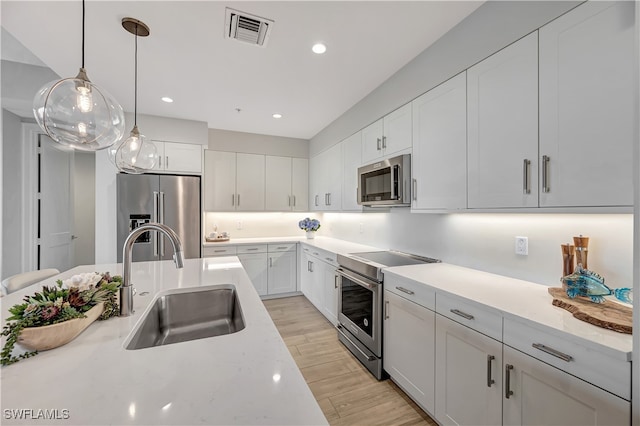 kitchen with light hardwood / wood-style floors, sink, appliances with stainless steel finishes, white cabinets, and pendant lighting