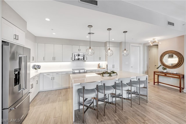 kitchen featuring a center island, stainless steel appliances, white cabinetry, decorative light fixtures, and light hardwood / wood-style flooring