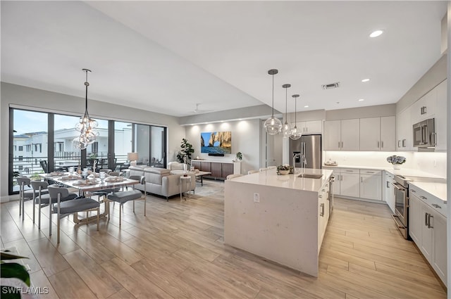 kitchen with light hardwood / wood-style flooring, an island with sink, white cabinetry, appliances with stainless steel finishes, and decorative light fixtures