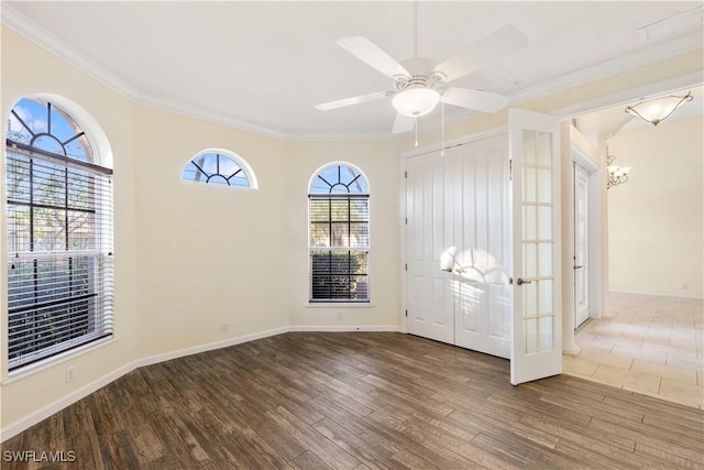 spare room featuring wood-type flooring, ornamental molding, ceiling fan with notable chandelier, and french doors