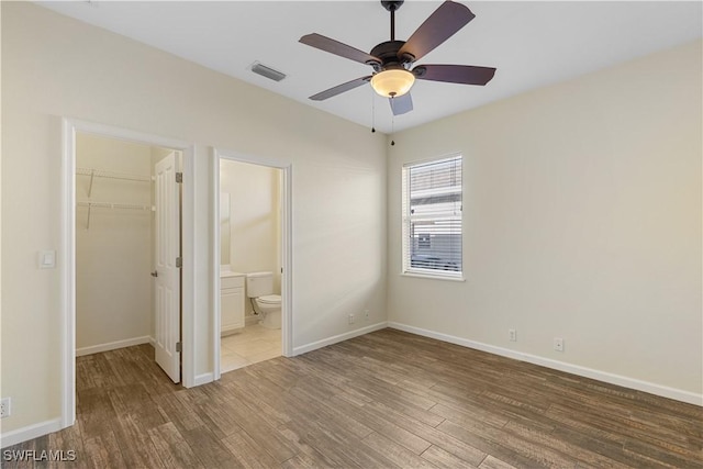 unfurnished bedroom with ensuite bathroom, a walk in closet, wood-type flooring, a closet, and ceiling fan